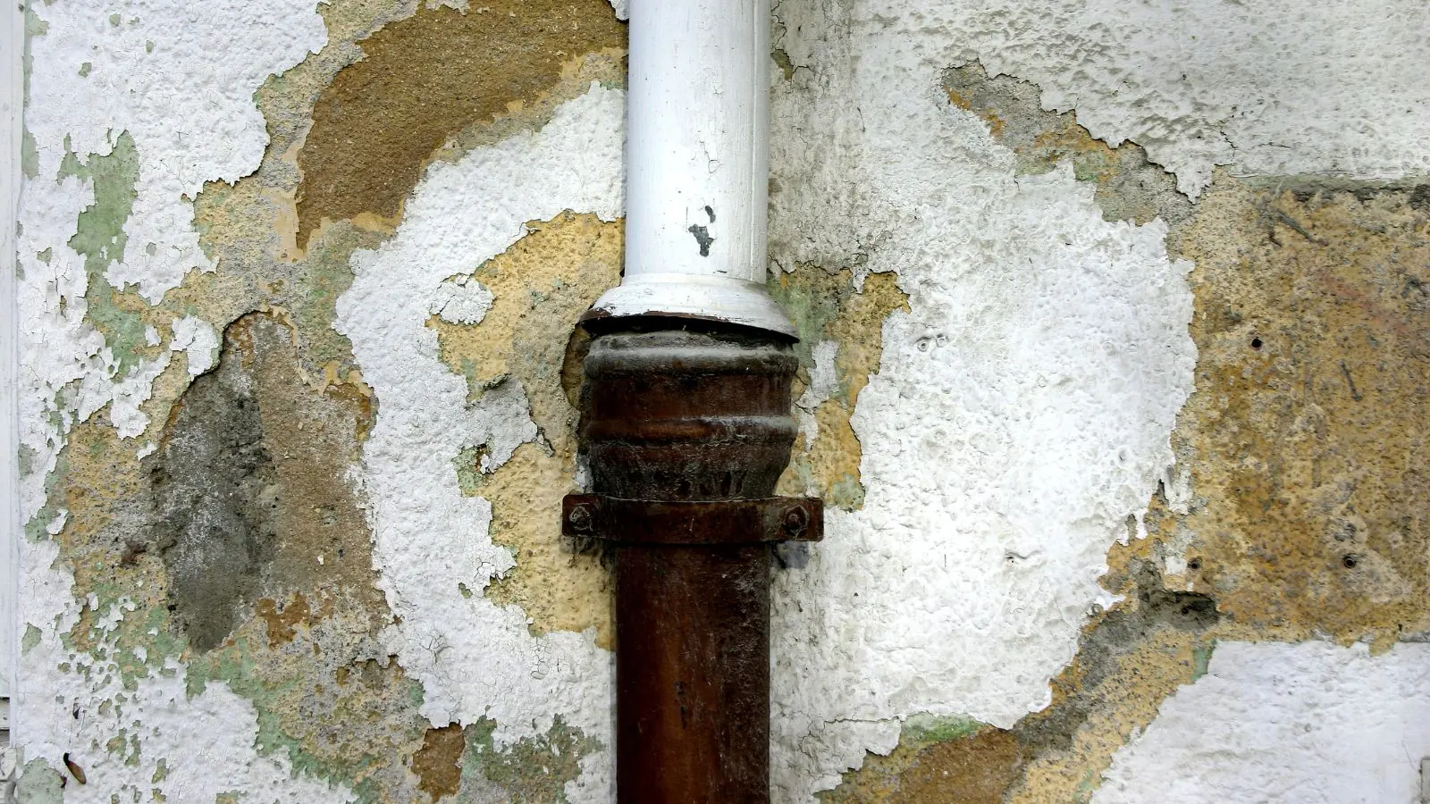 Water-damaged peeling drywall around a pipe