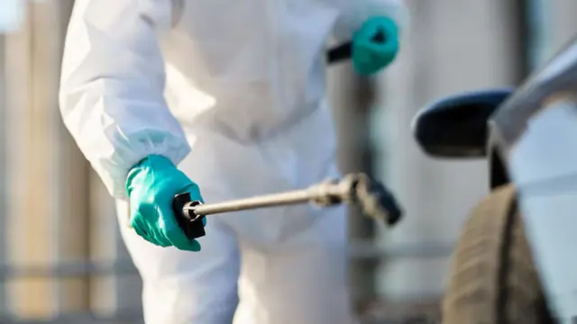 Worker in a white suit and teal gloves operating mold treatment equipment