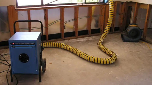 Desiccant dehumidifier with a yellow duct and an air mover beside exposed wall studs